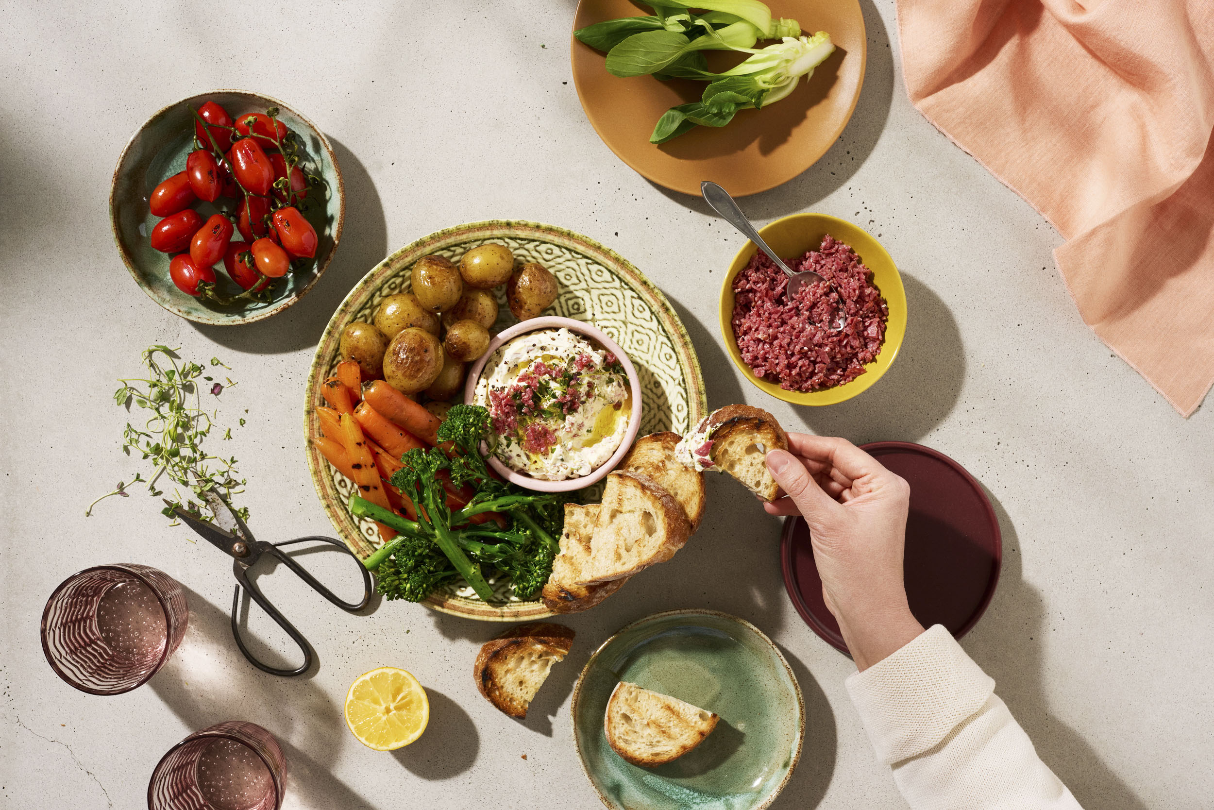 Ylhäältä kattauksessa vihanneksia, kirsikkatomaatteja, paistettuja perunoita, hummusta, jauhelihaa sekä leipää.
