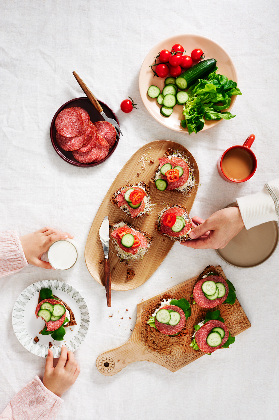 Alkupala-annoksia pöydällä: salami-sämpylöitä kurkku- ja tomaattiviipaleilla sekä vihreää salaattia.