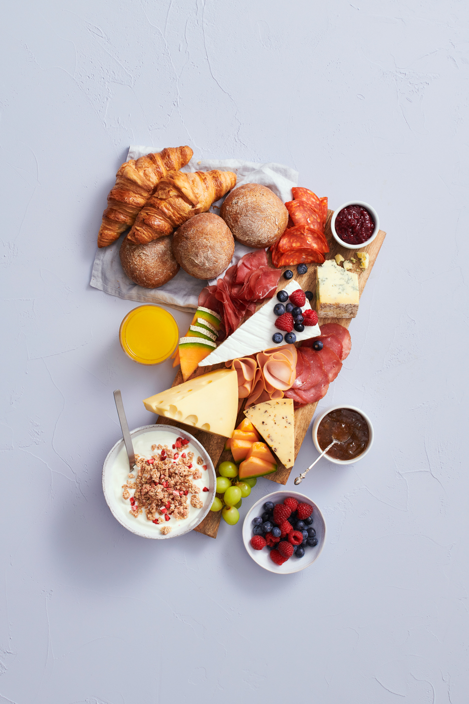 Charcuterie-lautanen: croissantteja, ruisleipää, juustoja, leikkeleitä, marjoja ja hedelmiä sekä jugurtti granolalla.