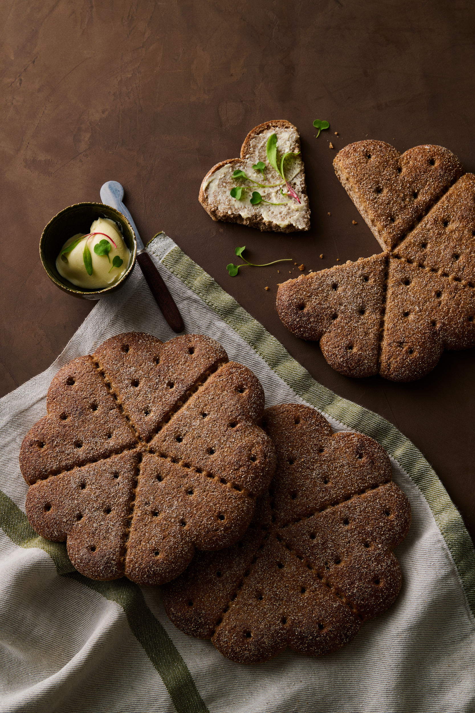 Sydämenmuotoiset täysjyvänäkkileivät voin ja tuoreiden mikrovihreiden kera pöydällä.