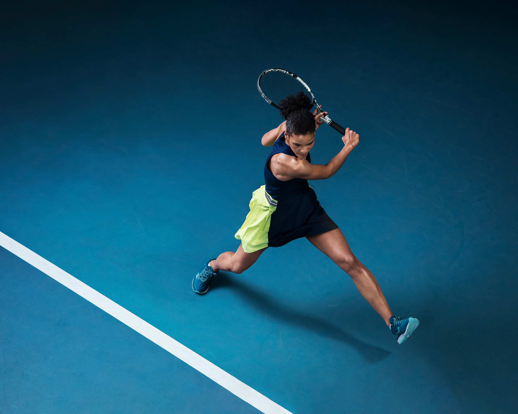 Naispelaaja iskee palloa sinisellä tenniskentällä dynaamisessa liikkeessä.
